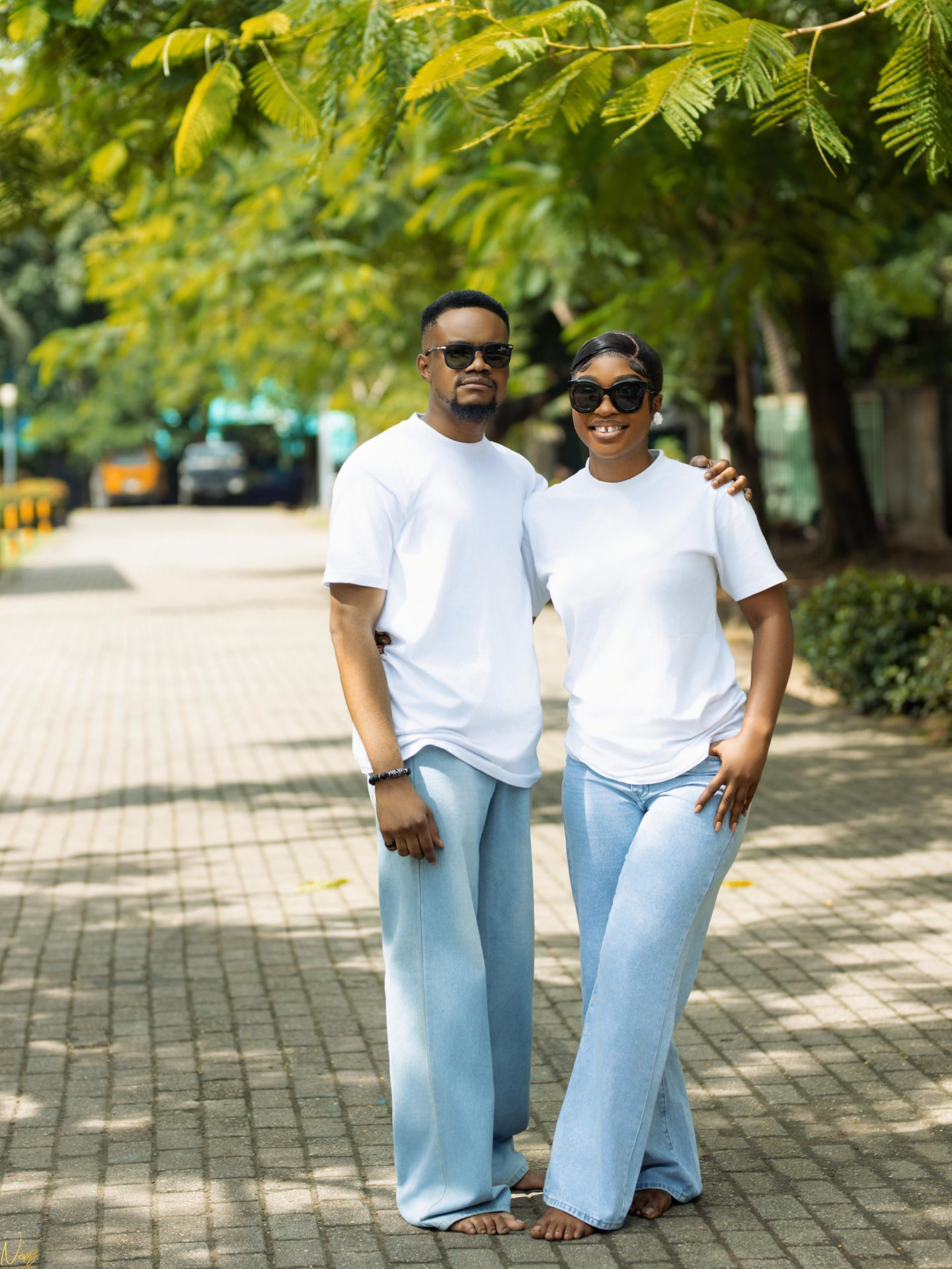 Kent and Iheoma in matching white t-shirts and jeans on a tree-lined walkway